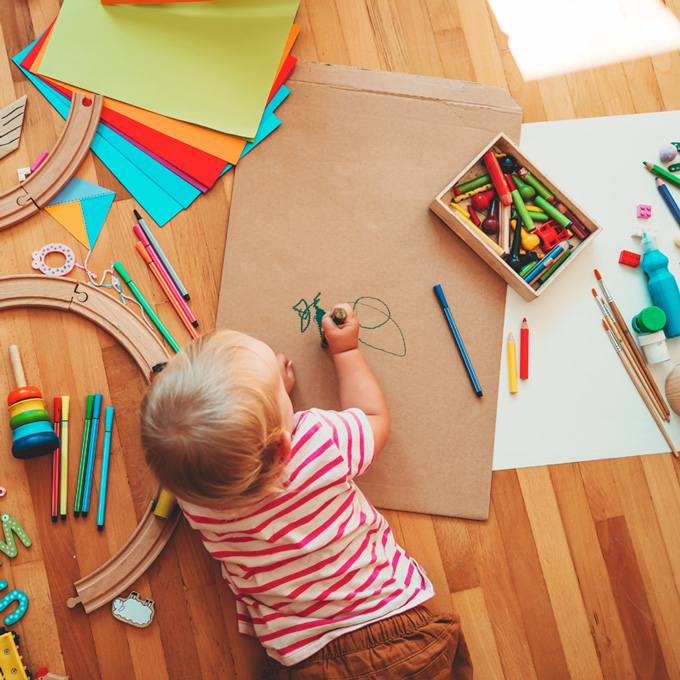L'enfant joue par terre et autour de lui se trouvent toutes sortes de jouets